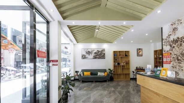 Un espace d’accueil moderne avec un comptoir de réception en bois, un canapé vert agrémenté de coussins, un grand tableau accroché au mur et une porte vitrée donnant sur l’extérieur.