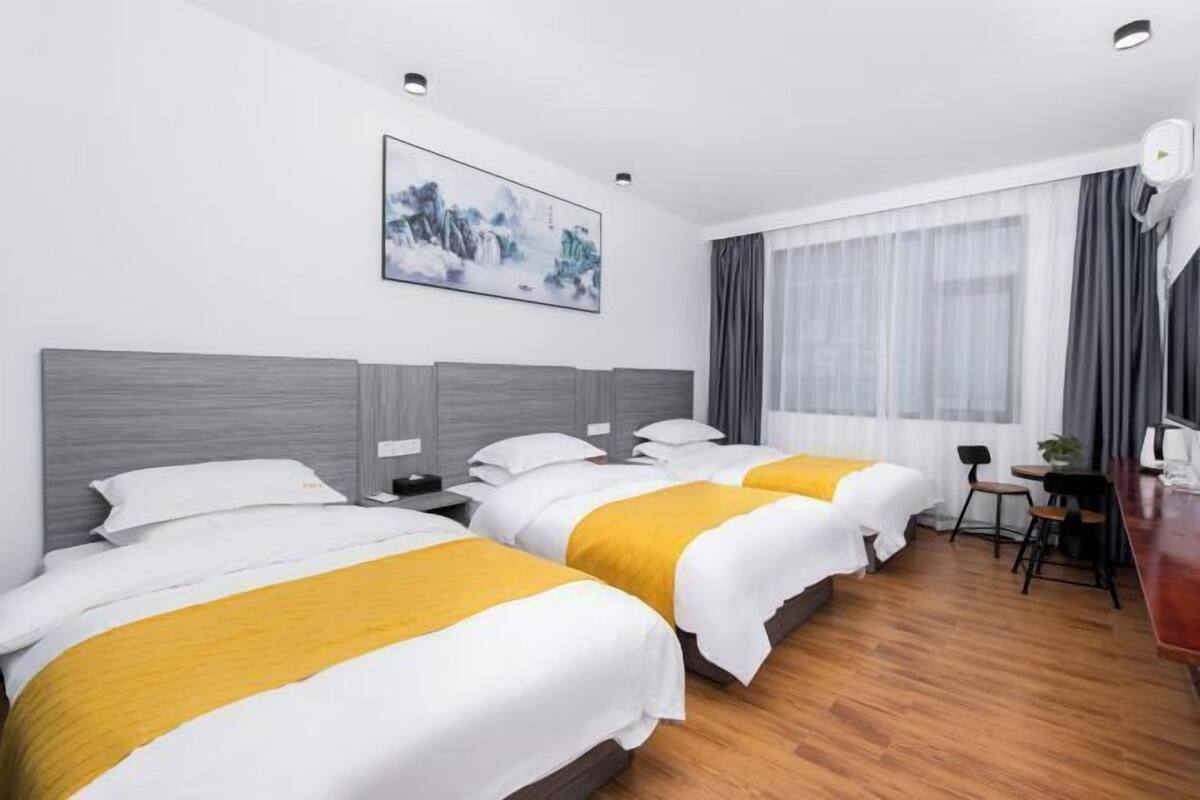 Ein Hotelzimmer mit drei Betten, einem Schreibtisch und einem großen Fenster mit Vorhängen.