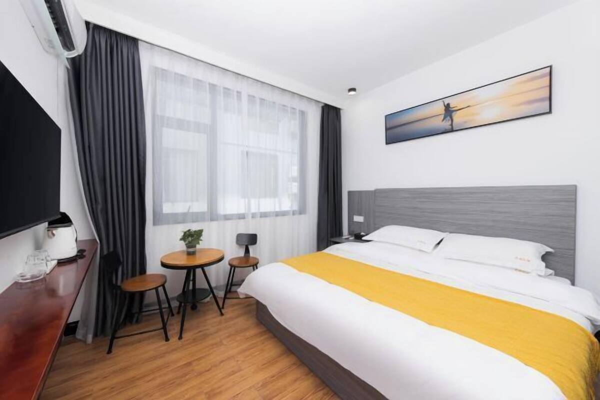 Ein Hotelzimmer mit einem Bett, einem Schreibtisch, einem Sessel, einem kleinen Tisch mit Pflanze und einem fenster mit Vorhängen.