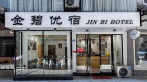 L’entrée d’un hôtel, avec des portes en verre, une enseigne indiquant le nom de l’hôtel, et quelques scooters garés à l’extérieur.