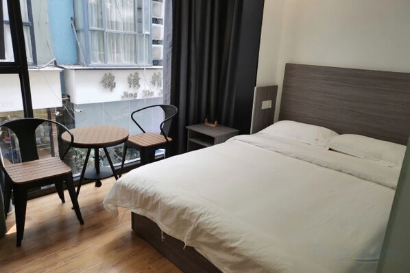 A hotel room with a bed, a small table, two chairs, a window with curtains, and a view of the outside.