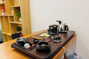 A wooden table with a tray holding various black ceramic items, including a teapot, cups, and a small bowl.
