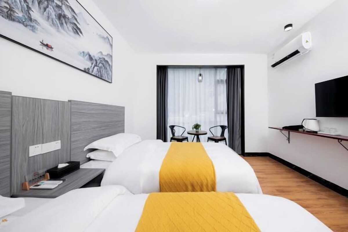 Une chambre d’hôtel avec deux lits, un bureau, une chaise, une télévision et un tableau au mur.