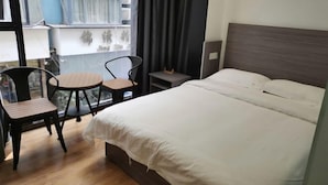 Une chambre d’hôtel avec un lit, deux chaises, une petite table et une fenêtre avec des rideaux.