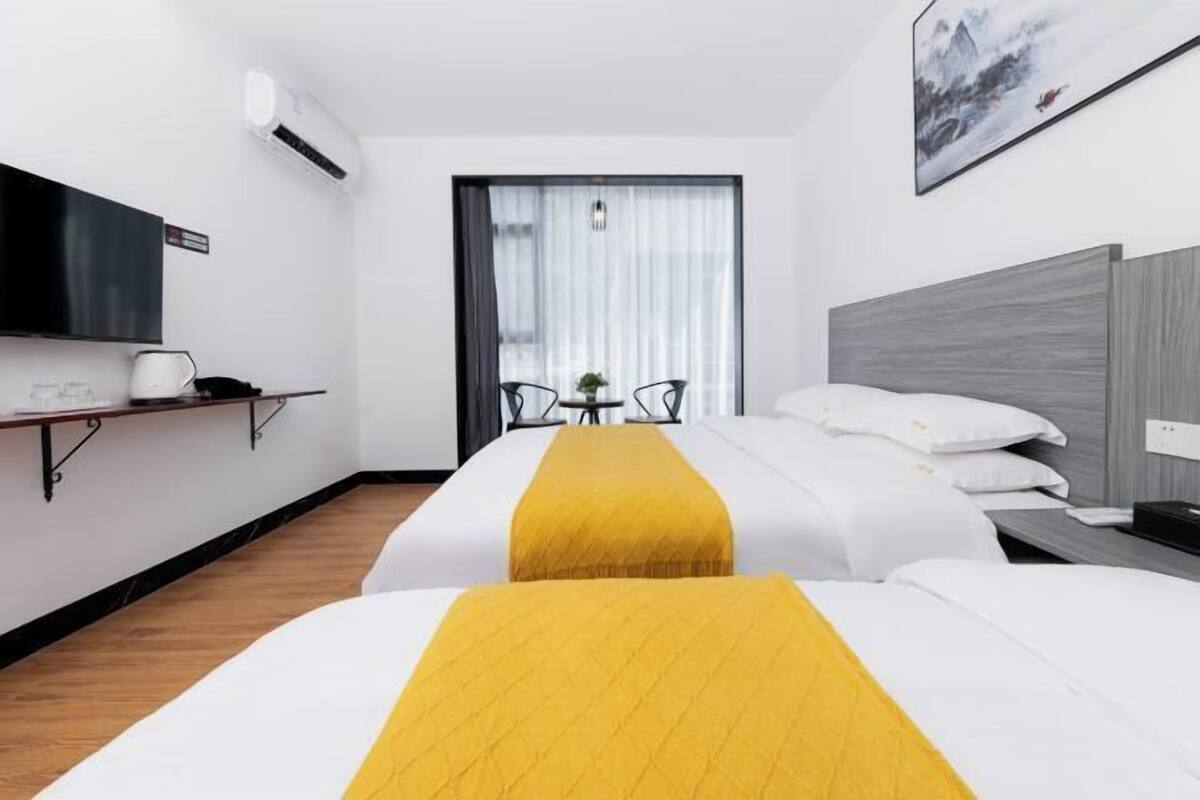 Ein Hotelzimmer mit zwei Betten, einem Fernseher, einem Schreibtisch und einem Fenster mit Vorhängen.