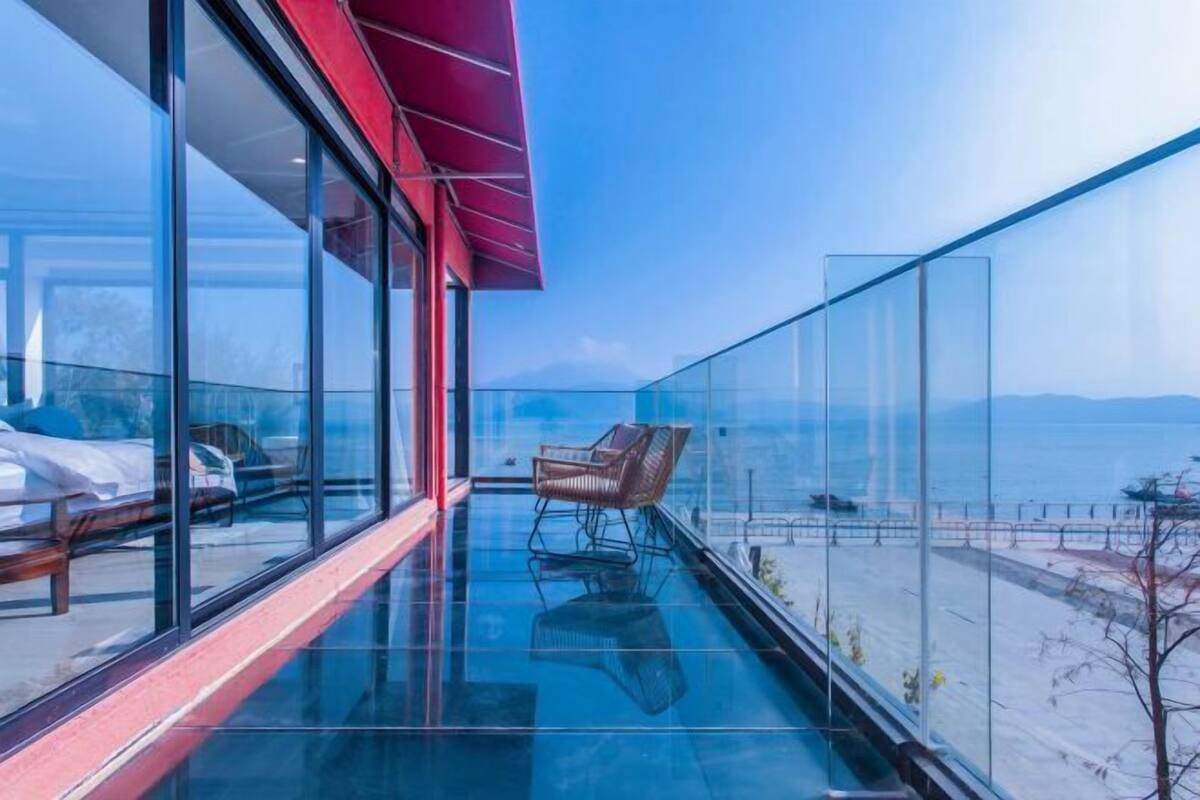 A modern balcony with a glass floor, a wooden chair, and a view of the sea.