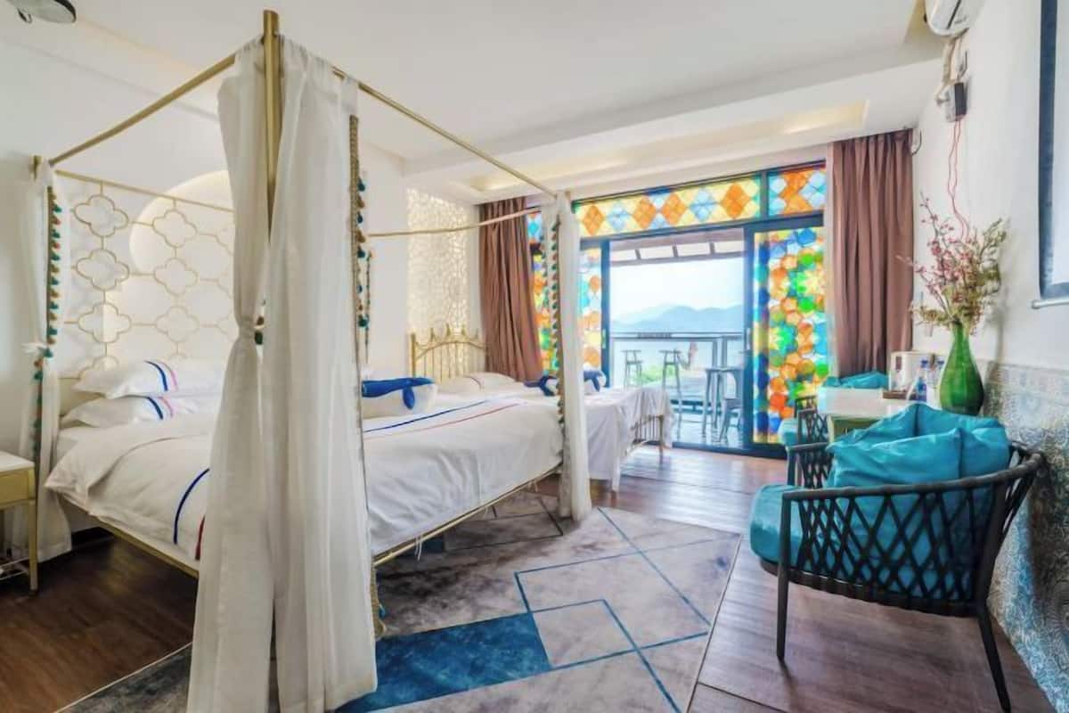 A hotel room with a four-poster bed, a balcony with a view, and a seating area with a table and chairs.