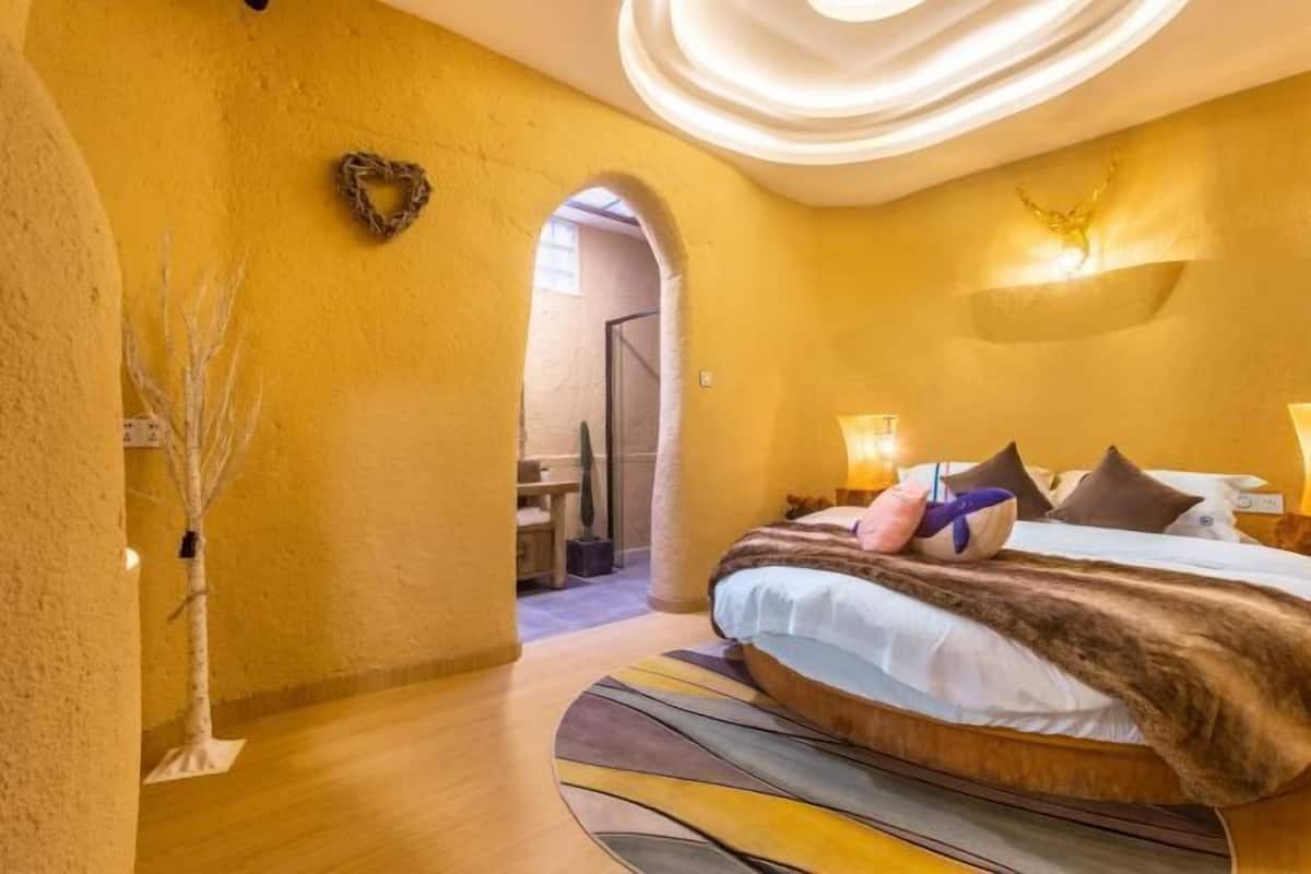 A bedroom with a large bed, a heart-shaped decoration on the wall, and a circular light fixture above the bed.