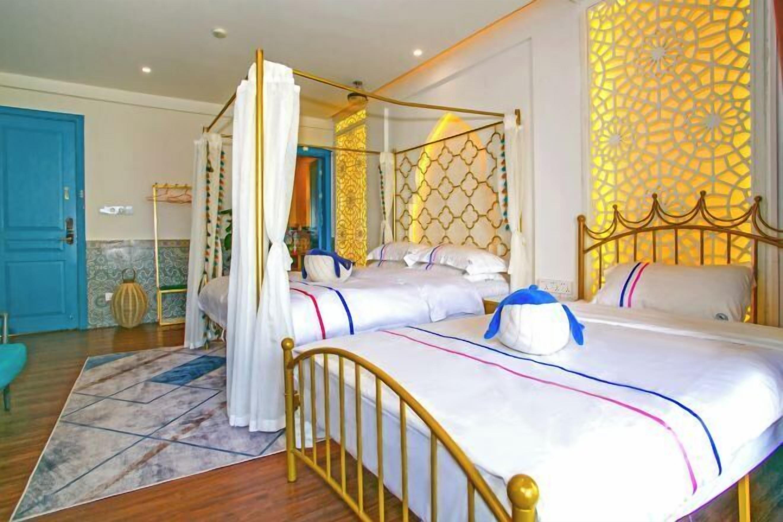 A four-poster bed with white linens and a gold frame, a blue door, and a patterned wall.