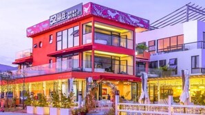 Un hotel moderno con fachada roja, amplias ventanas y zona de estar al aire libre.