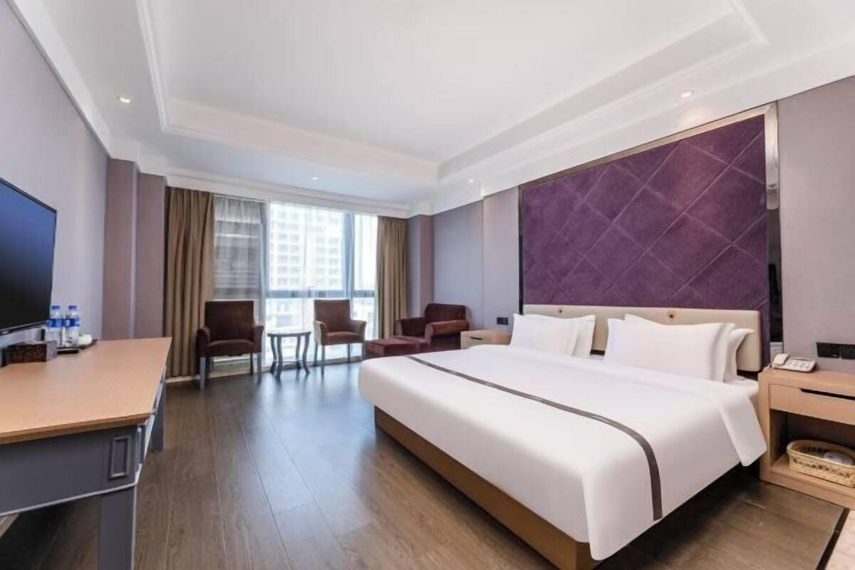 A hotel room with a large bed, a desk, a TV, and a view of the city.
