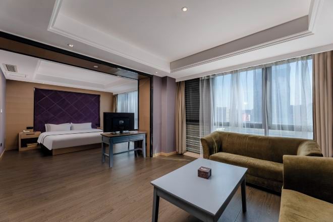 A hotel room with a bed, a TV, a sofa, a coffee table, and large windows.