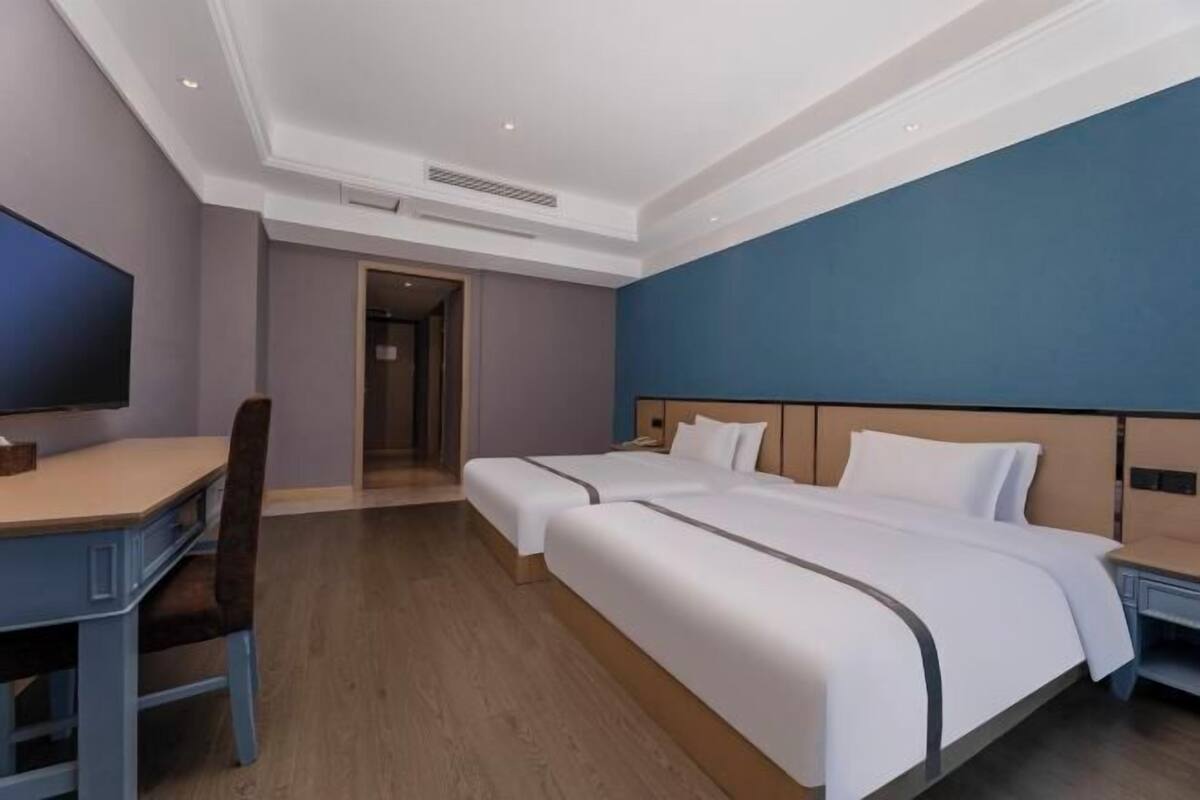 A hotel room with two beds, a desk, and a TV.