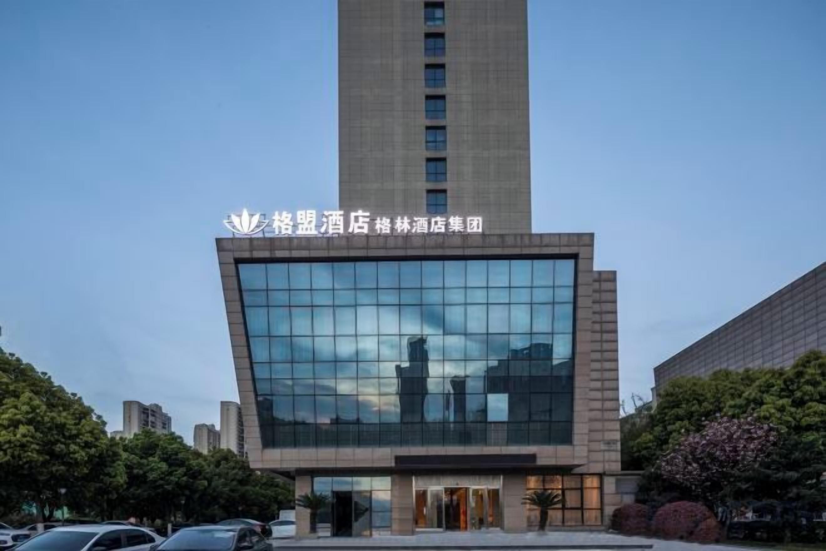 A modern hotel building with a prominent glass facade and a tall structure in the background.