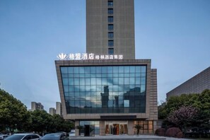 A modern hotel building with a prominent glass facade and a tall structure in the background. - GreenTree Alliance Hotel (Huzhou South Taihu Hospital) (Huzhou)