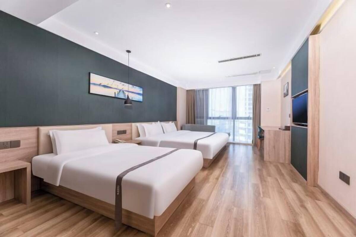 A modern hotel room with two beds, a large window, and a TV.