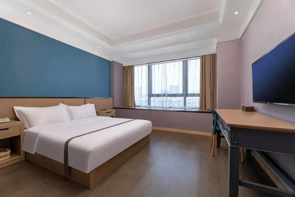 A hotel room with a bed, desk, and large window.