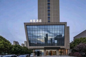 A modern hotel building with a prominent glass facade and a tall structure to the left. - GreenTree Alliance Hotel (Huzhou South Taihu Hospital) (Huzhou)