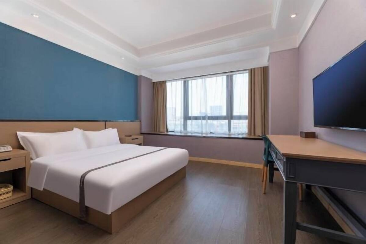 A hotel room with a bed, a desk, a TV, a window with curtains, and a city view.