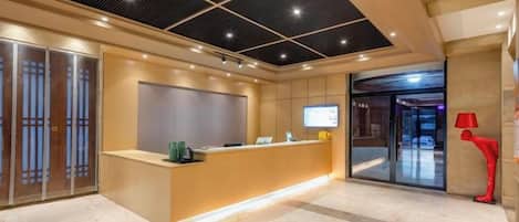 A hotel reception area with a reception desk, a digital screen, and a red sculpture.