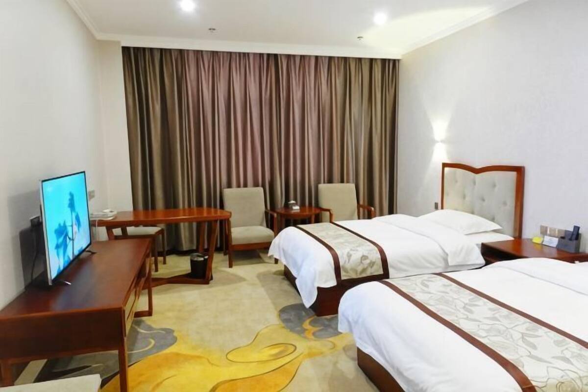Habitación de hotel con dos camas, televisión, escritorio y una silla.