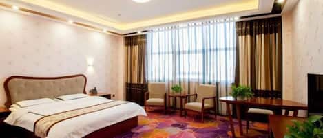 A hotel room with a large bed, a desk, two chairs, and a window with curtains.