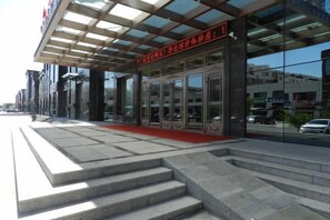 A building with a glass facade, a red carpet entrance, and a set of stairs leading to the entrance. - Di Jing Hotel (Xilinhot)