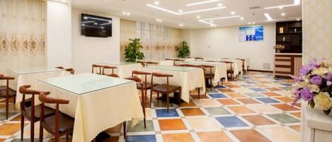 A dining area with tables and chairs, a television mounted on the wall, and a patterned floor.