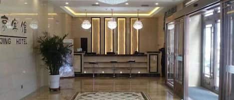 A hotel lobby with a reception desk, a chandelier, and a patterned floor.