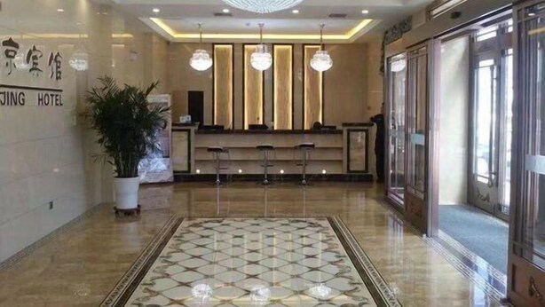 Eine Hotelhalle mit einer großen Chandelüster, einem Empfangstresen und einem gefliesten Boden.
