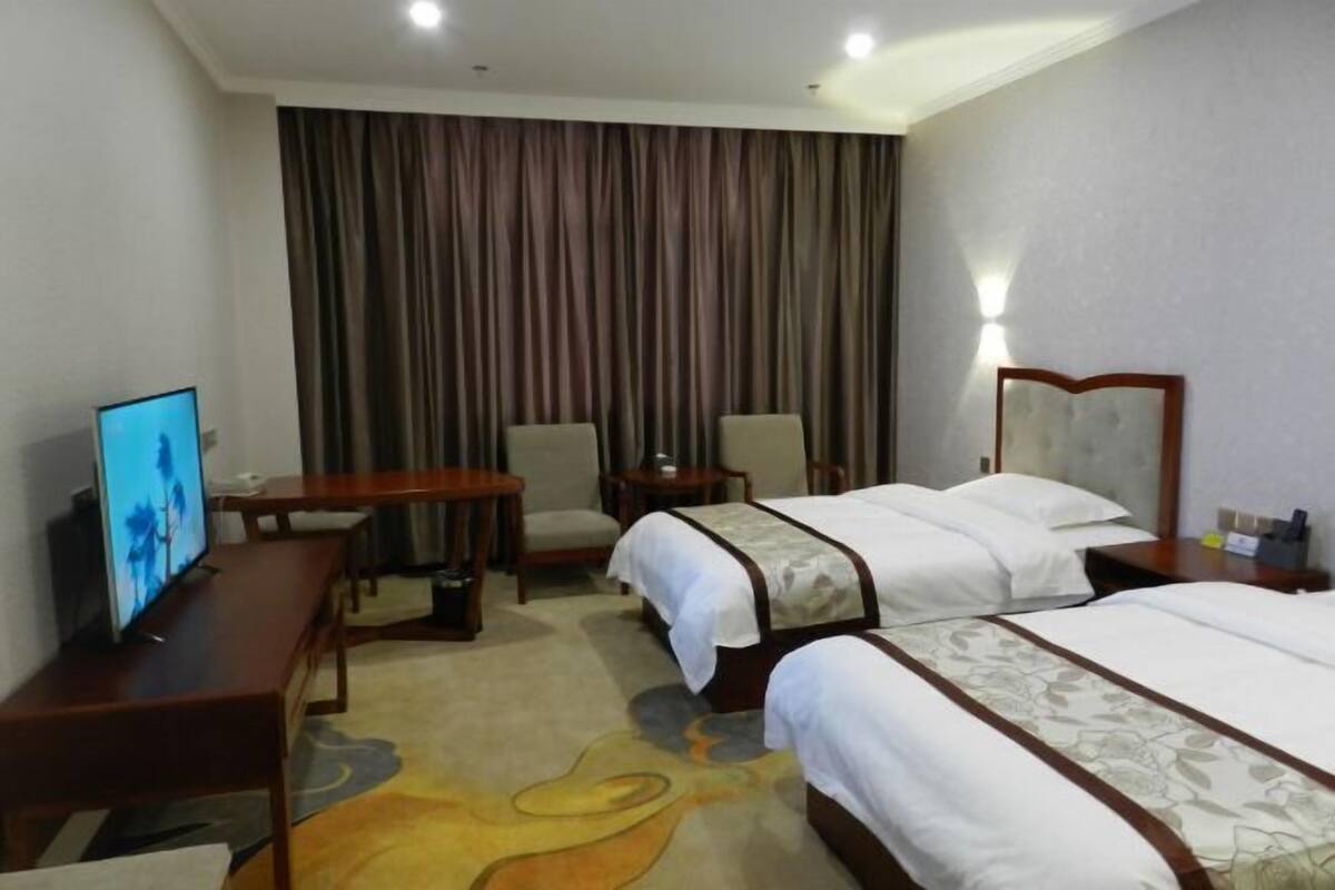 Una habitación de hotel con dos camas, televisión, escritorio, silla y cortina.