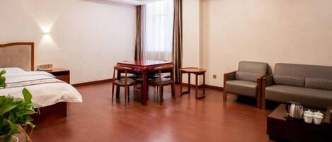A hotel room with a bed, a dining table with chairs, a sofa, and a small table with a teapot.