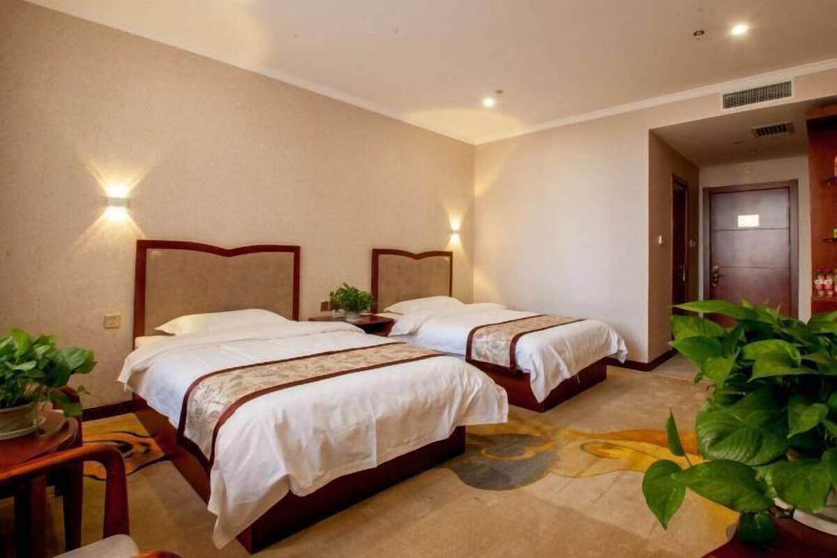 Habitación de hotel con dos camas, cada una con cabecero y mesitas de noche. Se observan luces fijadas en la pared y una puerta.