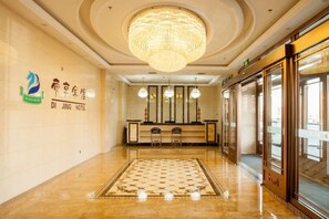 A hotel lobby with a chandelier, reception desk, and a check-in counter.