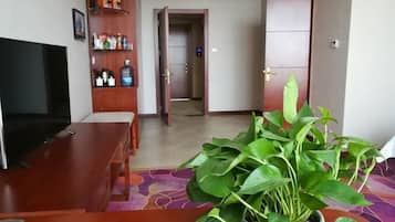 Una sala de estar con televisor, una mesa de madera, una planta en maceta y una puerta que da a otra habitación.