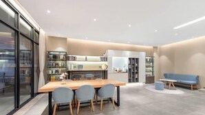 A modern interior with a dining area featuring a wooden table and four chairs, a kitchen with built-in appliances, and a seating area with a blue sofa and a small round table. - Homeinn · neo (Taiyuan Railway Station Shuangta East Street) (Taiyuan)