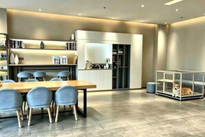 A modern dining area with a wooden table and chairs, a kitchen in the background, and a pet cage with a dog. - Homeinn · neo (Taiyuan Railway Station Shuangta East Street) (Taiyuan)