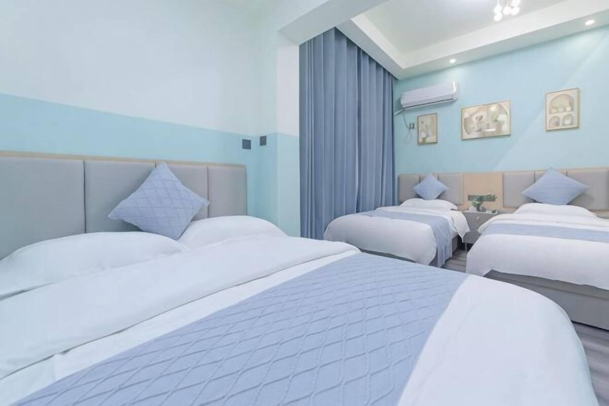 Una habitación de hotel con dos camas, un ventanal con cortinas, un televisor de pantalla plana y un aire acondicionado instalado en la pared.
