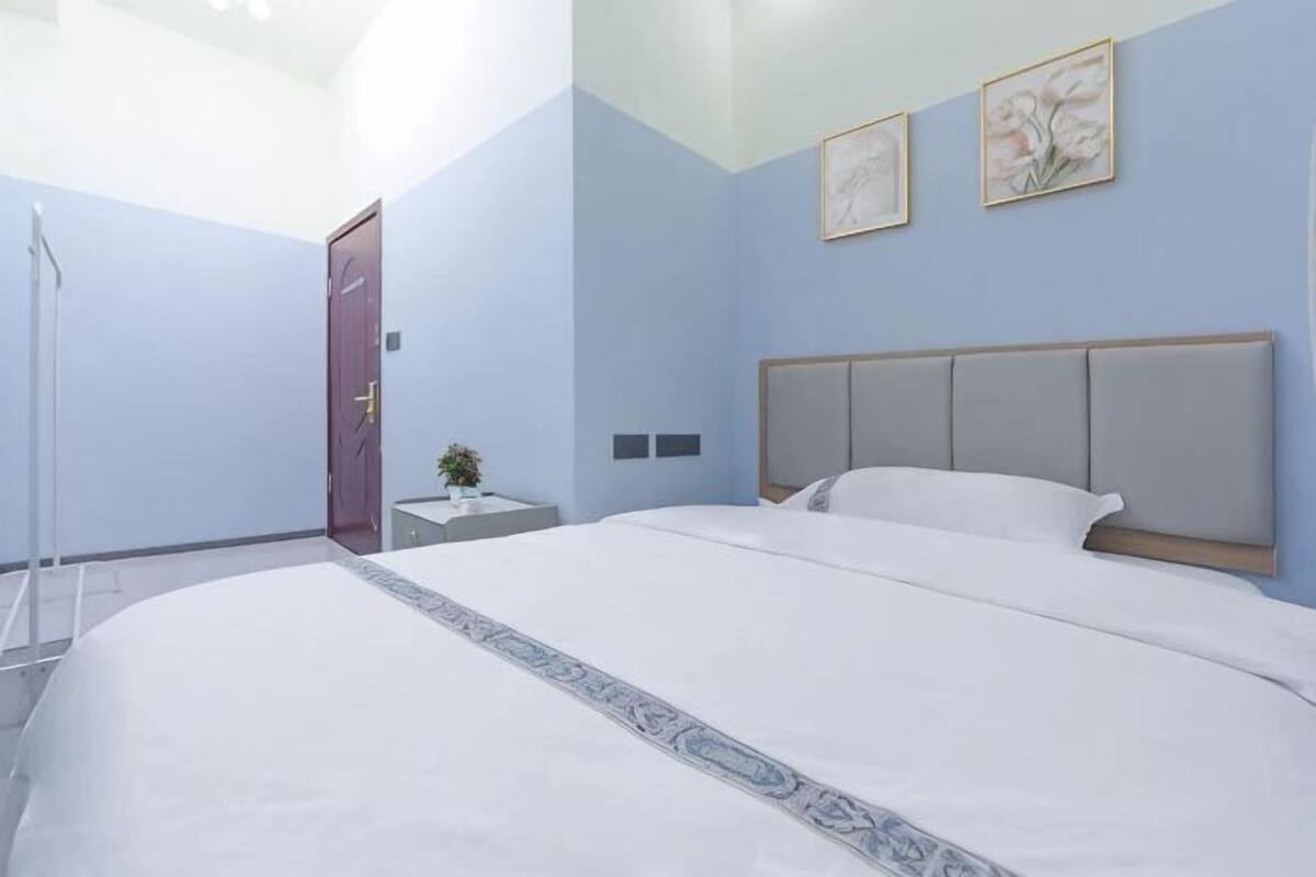 Una habitación de hotel con una cama grande, una mesita de noche, una pequeña mesa con una planta y una puerta.