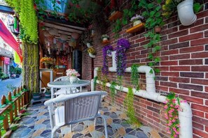 Une terrasse avec un mur en briques, des bordures blanches et diverses plantes.