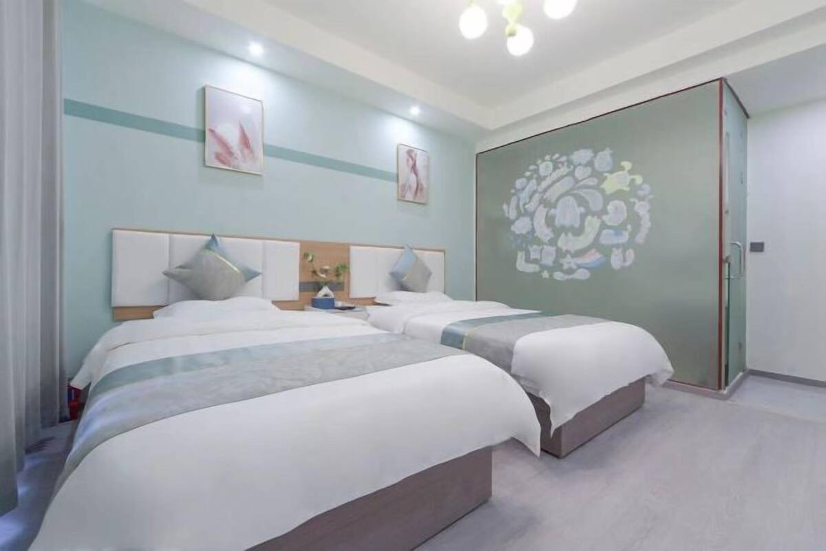 Habitación de hotel con dos camas, armario con puerta de vidrio y obras de arte en las paredes.