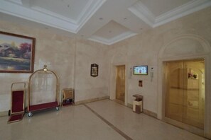 A lobby with a reception desk, a gold elevator, and a painting on the wall. - jinlouerhotle (Shenzhen)