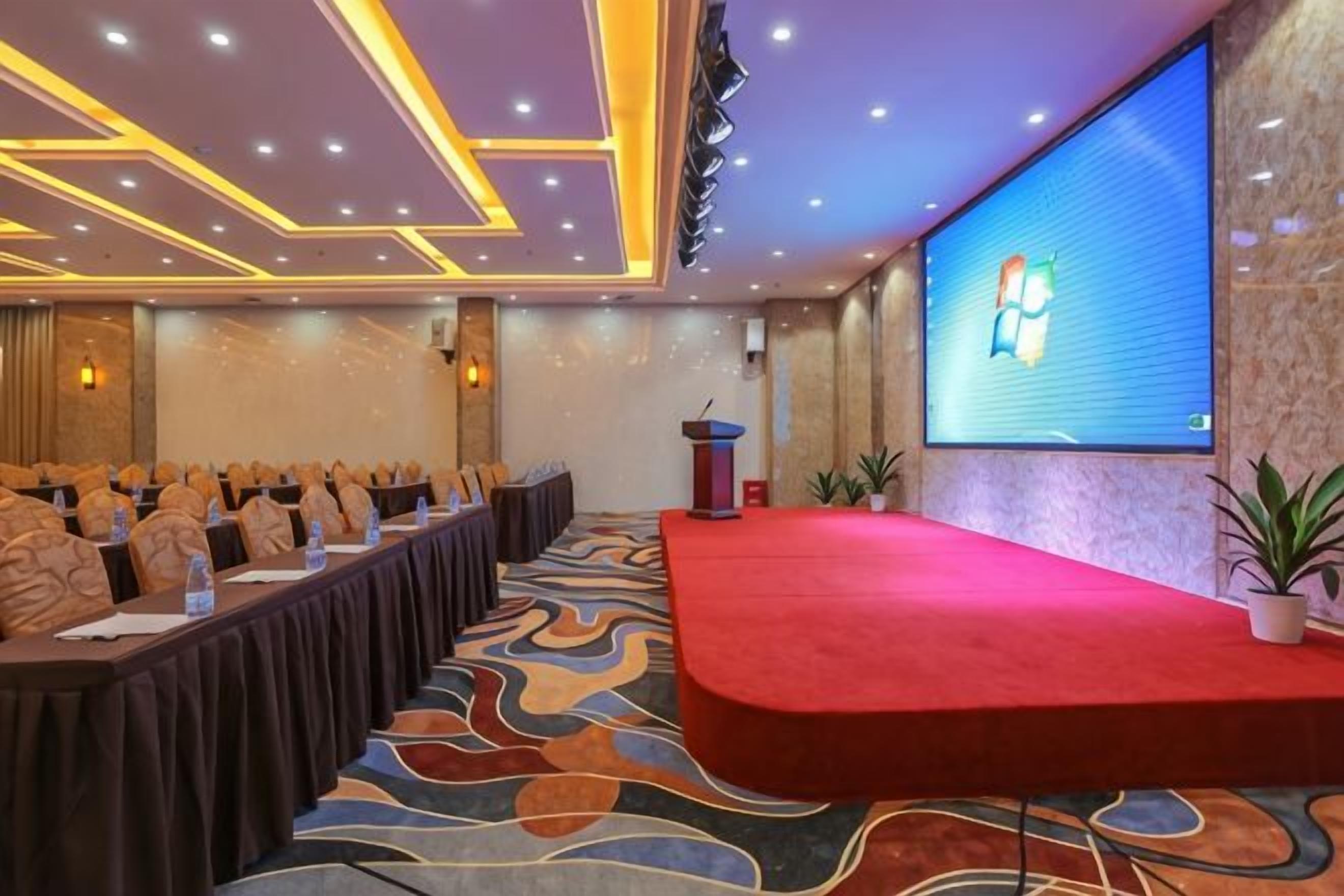 A conference room with a stage, a long table with chairs, and a large screen.
