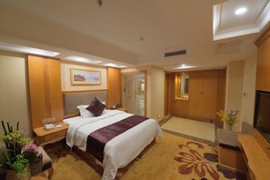 Ein Hotelzimmer mit einem großen Bett, einem Schreibtisch, einem Fernseher und einem durch eine offene Tür einsehbarer Badezimmer.