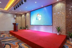 A conference room with a red carpeted stage, a large screen displaying a logo, and a podium. - jinlouerhotle (Shenzhen)