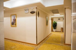 A hallway with patterned carpet, a potted plant, and a framed picture on the wall.