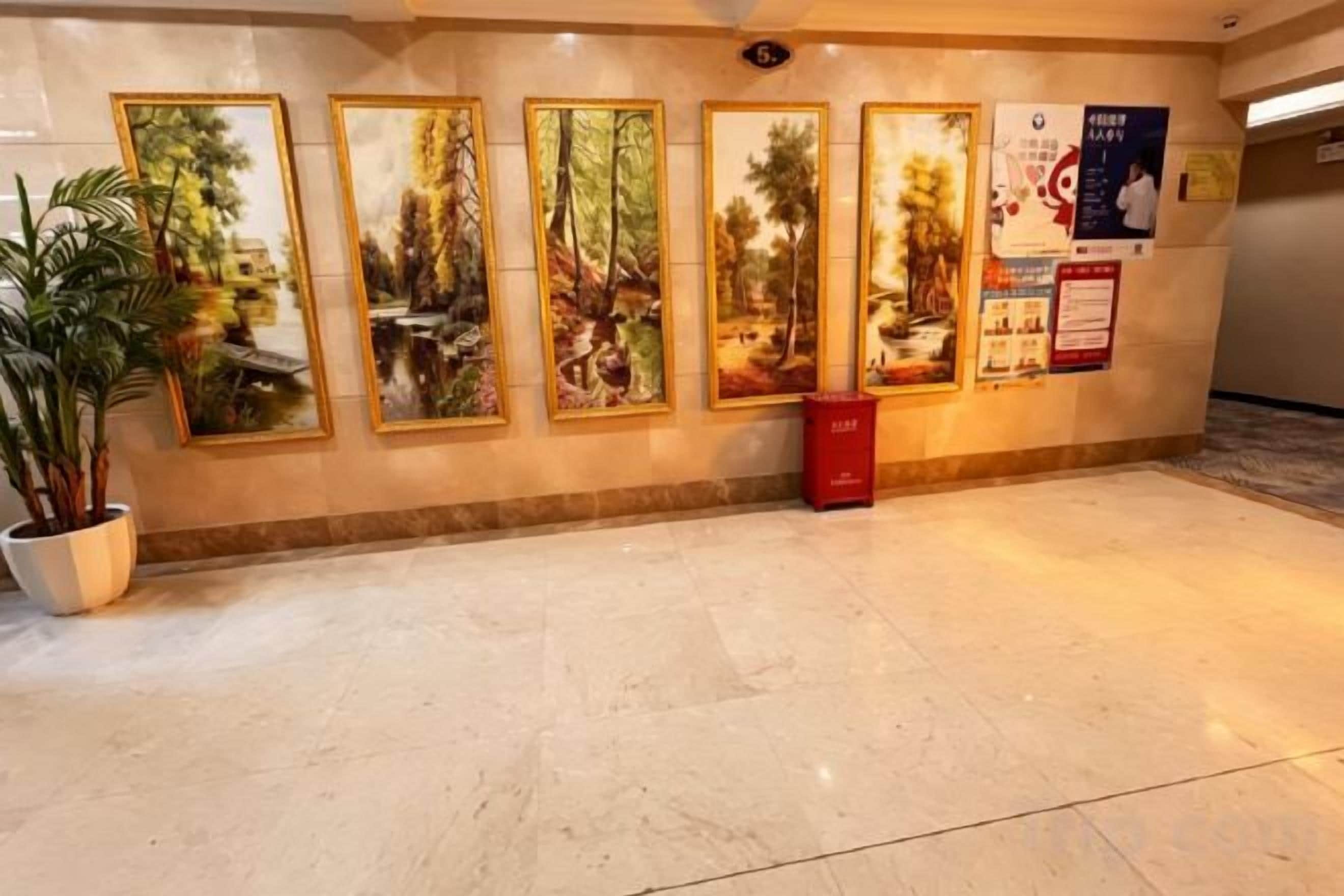 A hallway with framed pictures on the wall, a potted plant, and a red trash bin.