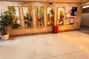 A hallway with framed pictures on the wall, a potted plant, and a red trash bin. - Vernal Hotel (Shenzhen Shiyan Shilongzi Branch) (Shenzhen)
