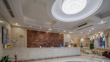 A hotel lobby with a reception desk, a large decorative wall, a chandelier, and a patterned floor.