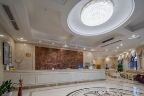 A hotel lobby with a reception desk, a large decorative wall, a chandelier, and a patterned floor. - jinlouerhotle (Shenzhen)